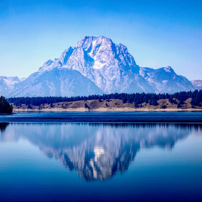 pexels-photo-2836719-2836719 A peaceful view of Grand Teton mountains reflected in a placid lake under a clear blue sky.